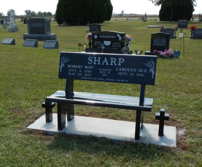 Black memorial bench and marker on a grassy cemetery plot under a cloudy sky.