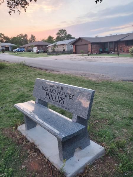 Stone bench memorial with plaque reading “No one lives forever,” beside a road at dusk
