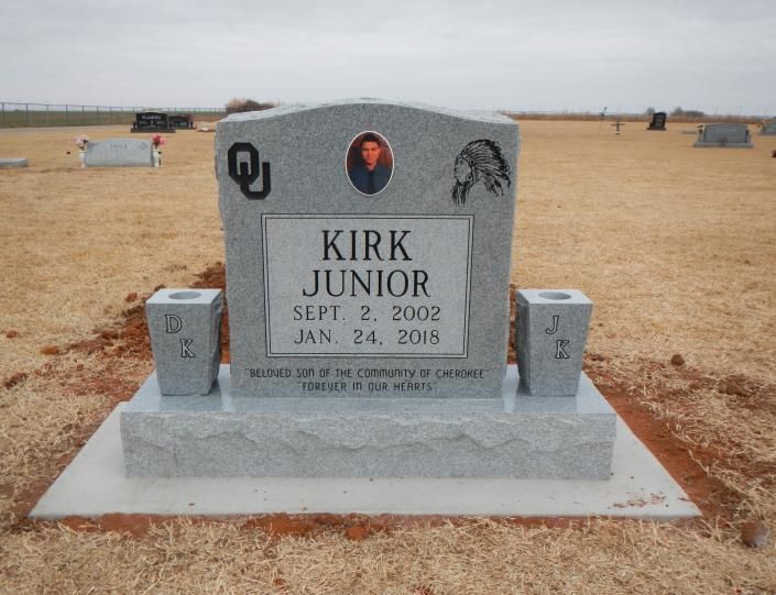 Gray gravestone for Kirk Junior with oval portrait, set in a cemetery field