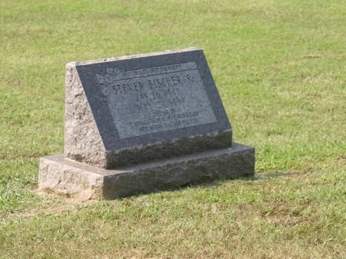Stone memorial plaque on a grassy lawn, with engraved text on a slanted base.