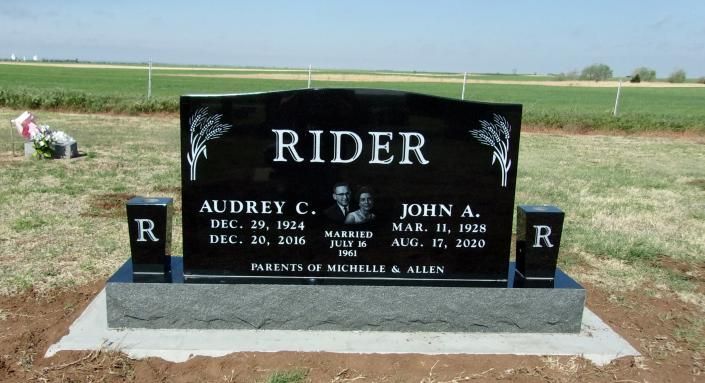 Black Rider memorial gravestone with gold lettering in a rural field, flanked by small marker stones