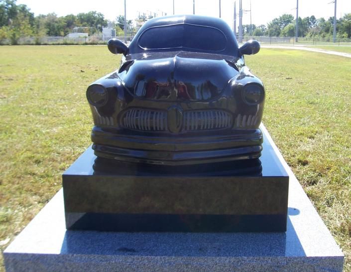 Black car sculpture on a pedestal in a grassy outdoor park