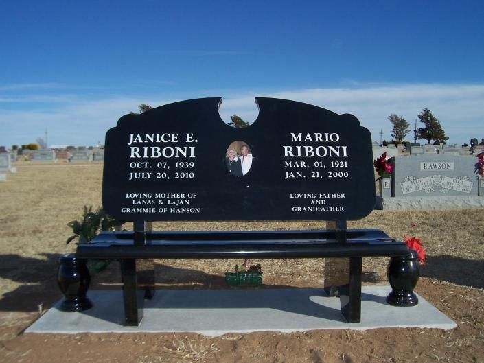 Black memorial bench grave marker with engraved names in a cemetery under a blue sky