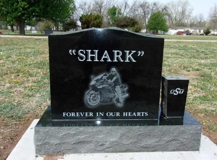Black motorcycle memorial headstone reading “SHARK” with “Forever in our hearts” in a grassy cemetery