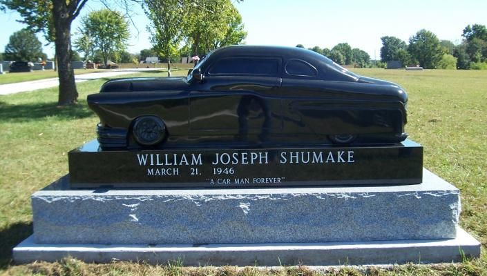 Black classic car sculpture on a grave marker in a grassy cemetery