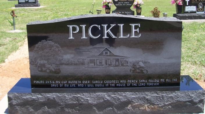 Black granite gravestone engraved “PICKLE” with a farmhouse scene and white lettering in a cemetery with grass.