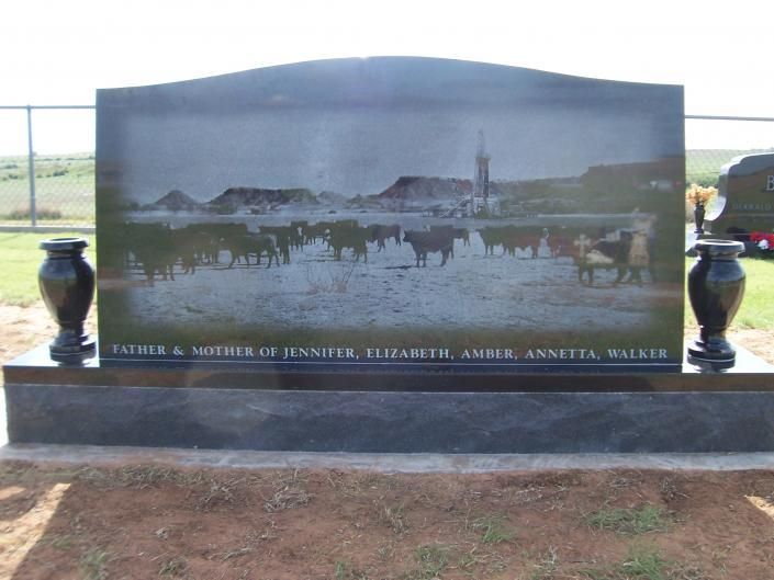 Large black memorial plaque with a ranch scene and cattle, flanked by two urns outdoors.