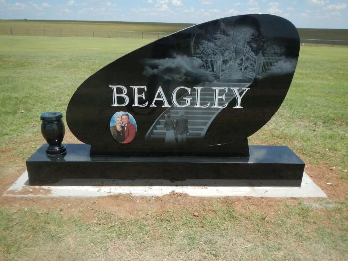 Black memorial headstone engraved “BEAGLEY” with a photo medallion, set on a grassy lawn.