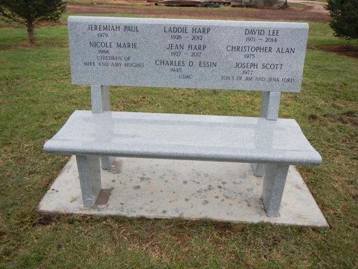 Engraved memorial bench on a concrete pad in a grassy park area