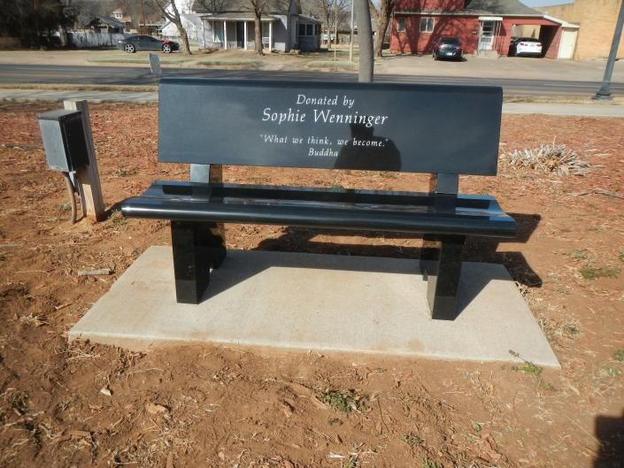 Memorial bench on concrete pad in a park, with engraved backrest and a small plaque beside it