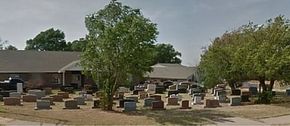 Outdoor memorial garden with rows of stone markers and trees in front of a low building