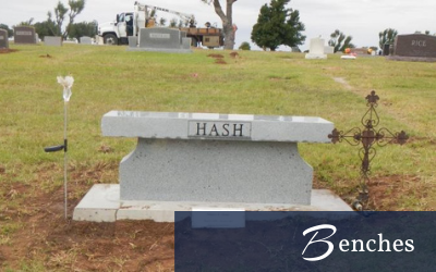 White grave bench marker engraved “HASH” in a cemetery with headstones and grass behind it
