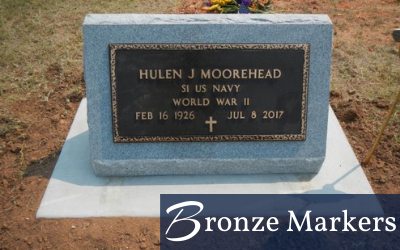 Bronze memorial plaque on a gray stone marker in a cemetery, engraved with dates and military service.