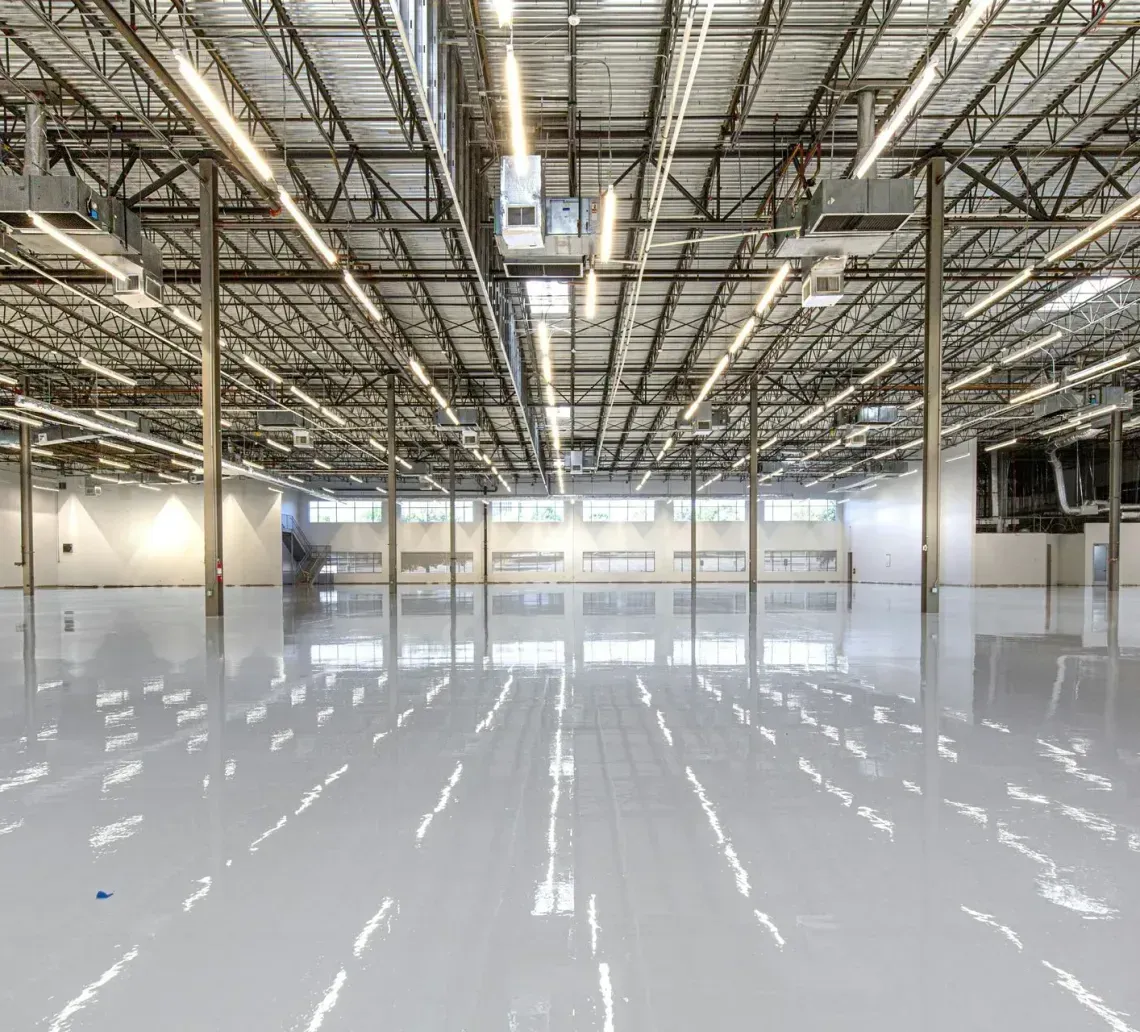 Empty warehouse interior with high metal ceiling, white walls, and polished concrete floor