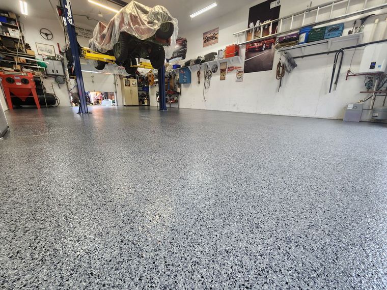 Person skateboarding in a garage with a speckled epoxy floor and tools on the walls