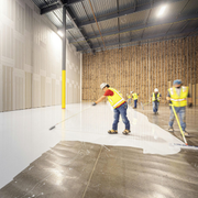 Workers pouring concrete on a warehouse floor inside a large industrial space.