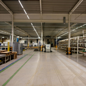 Empty factory interior with conveyor belts, machinery, and overhead lighting in a large warehouse