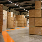 Warehouse aisle lined with stacked cardboard boxes and pallets under a metal roof