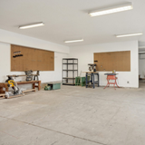 Empty white workshop with concrete floor, boarded windows, and tools along the walls