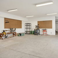 Empty white workshop with concrete floor, boarded windows, and tools along the walls