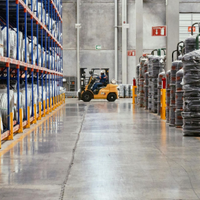 Warehouse aisle with stacked pallets, a forklift, and tall storage racks under bright lights
