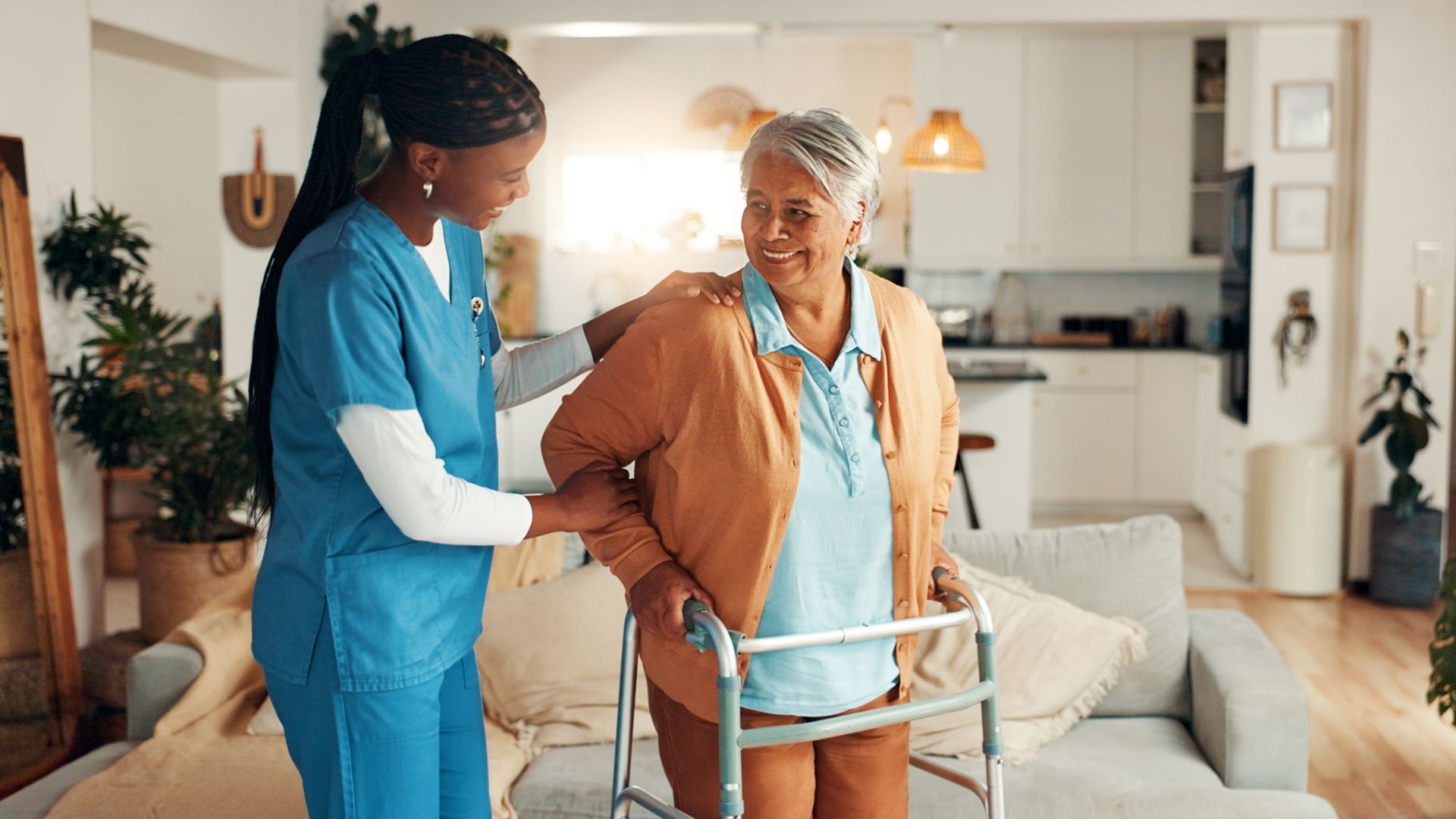 Caregiver helping a senior woman walk with a walker in a bright living room