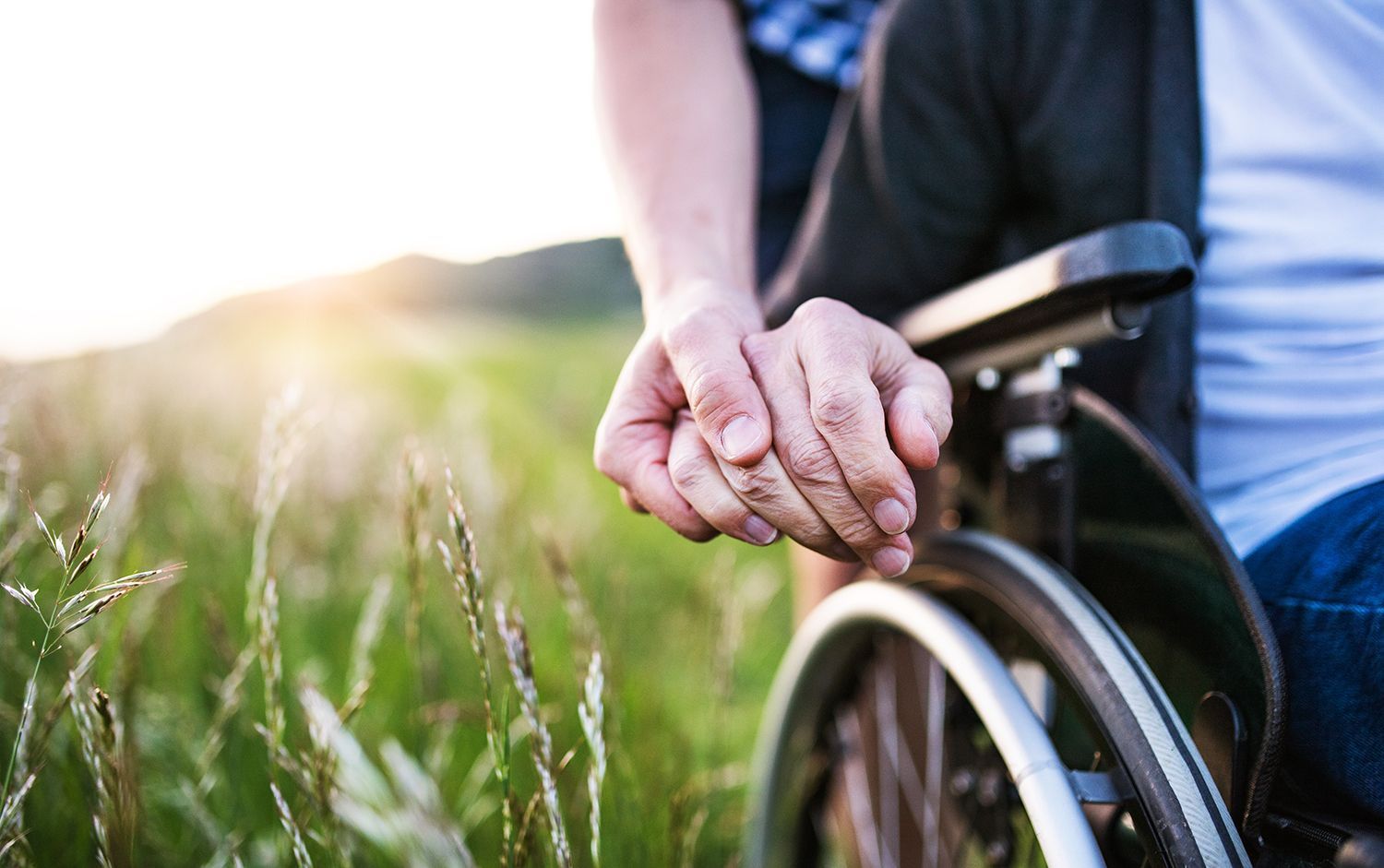 Person holding hands with someone in a wheelchair outdoors in a grassy field at sunset