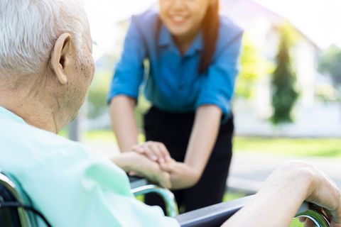 Caregiver holding an elderly person’s hand outdoors, with a caregiver kneeling and smiling in the background