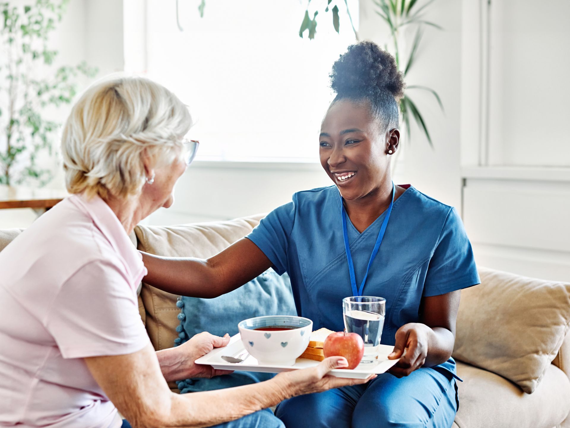 Caregiver serving tea to an elderly woman in a bright living room