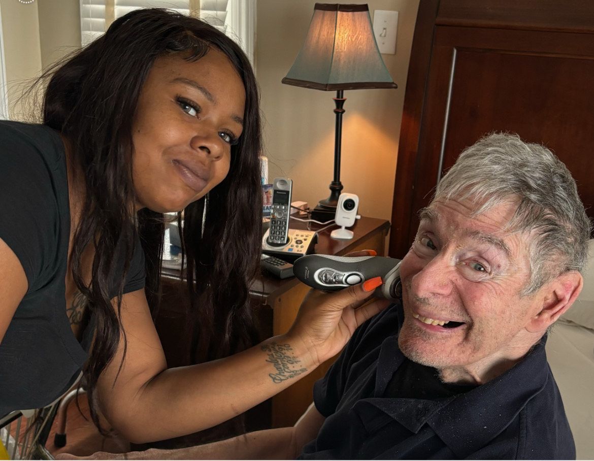 Caregiver comforting an elderly woman seated indoors, with a hand on her shoulder.