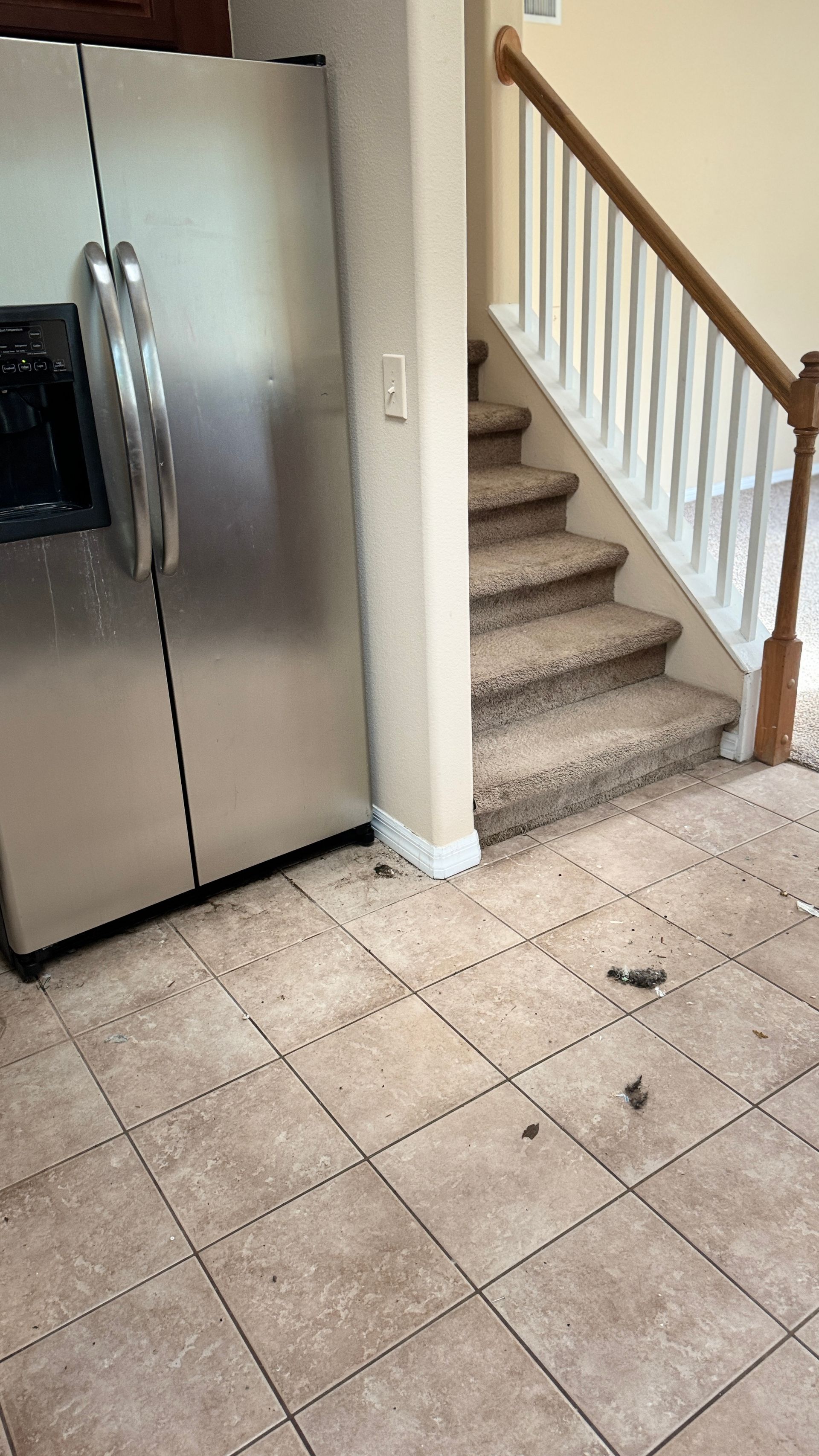 A stainless steel refrigerator is sitting next to a staircase in a kitchen.
