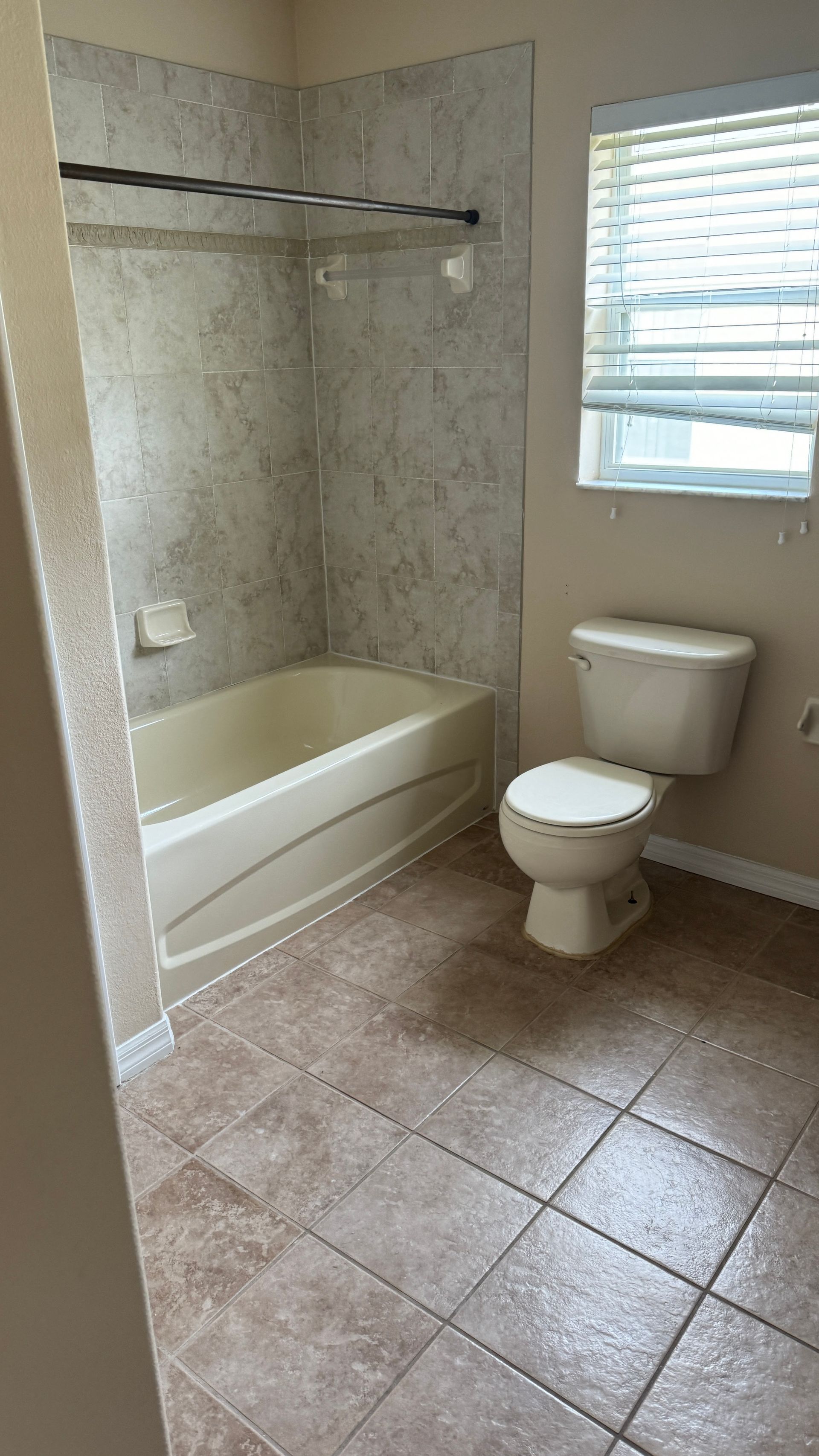 A bathroom with a toilet , bathtub and window.
