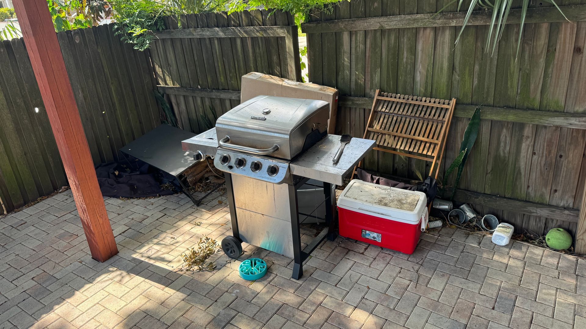 A grill is sitting on a brick patio next to a wooden fence.