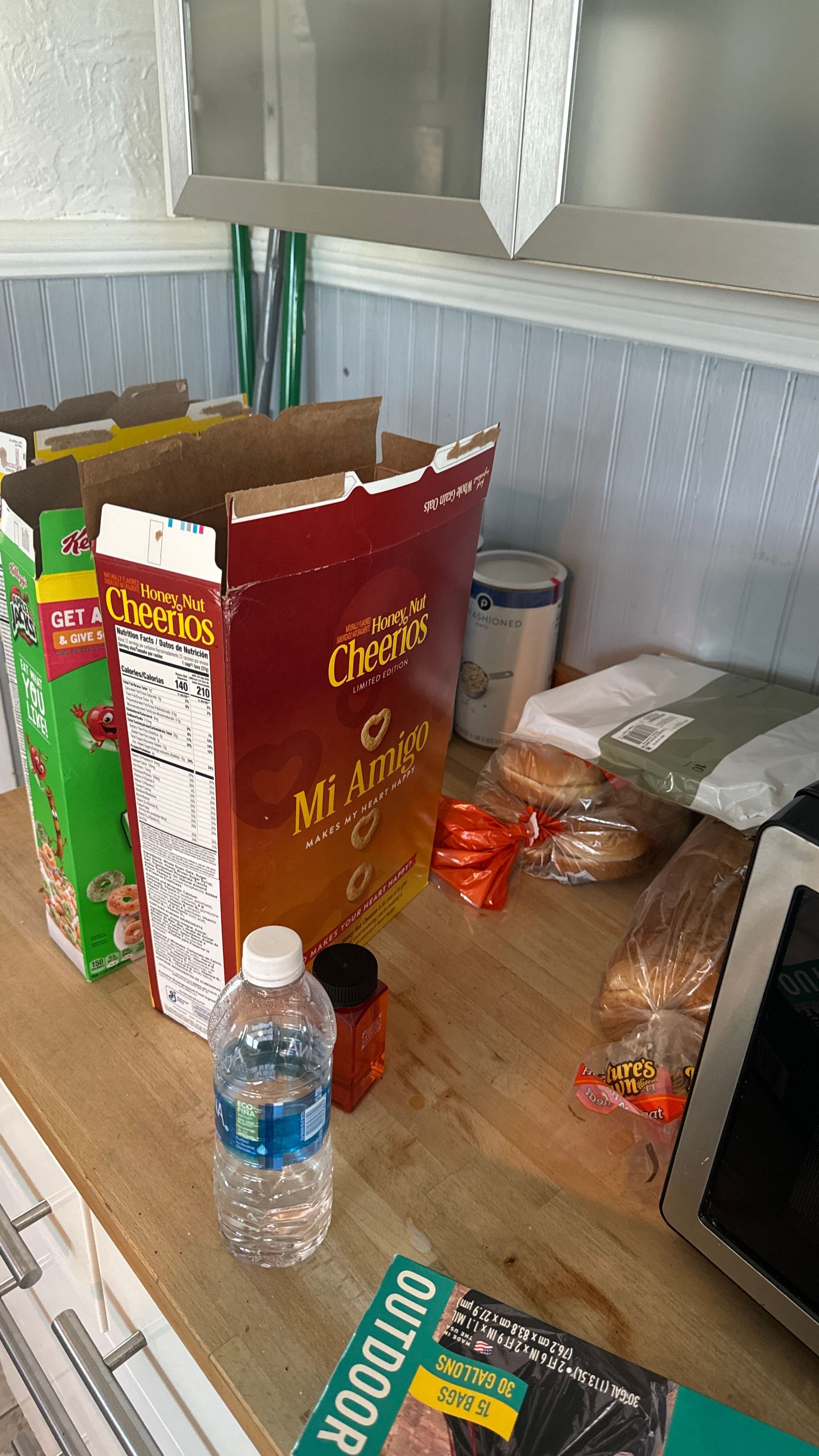 A box of cheerios sits on a kitchen counter next to a bottle of water.