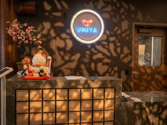 Warmly lit café counter with a glowing circular sign, flowers, and a small decorative statue on the left.
