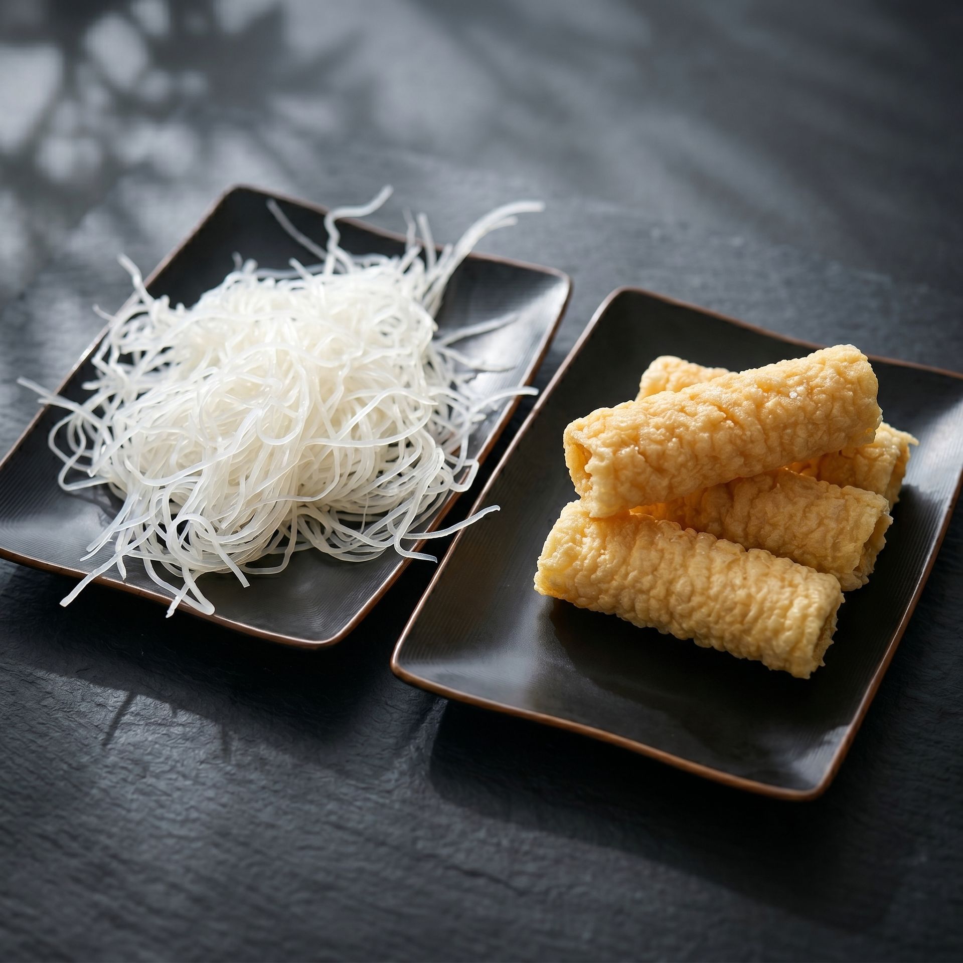 White shredded dessert and golden rolled pastries on two black plates on a dark table