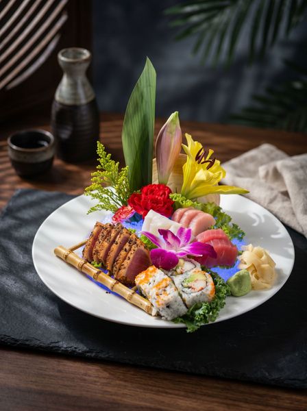 Sushi platter on a white plate with colorful sashimi and flowers on a dark tablecloth