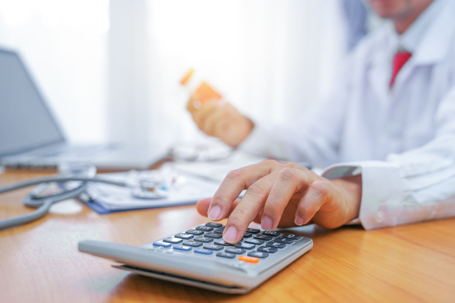 A doctor is using a calculator while holding a bottle of pills.