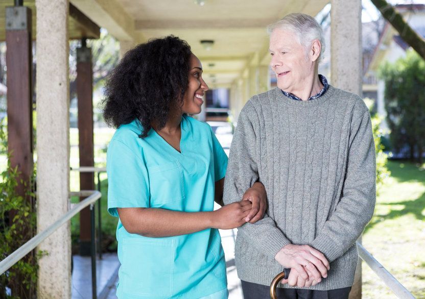Two people walking arm-in-arm on a covered outdoor walkway, smiling at each other.