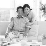 Couple sitting on a couch in a bright living room, smiling with tea cups on the table