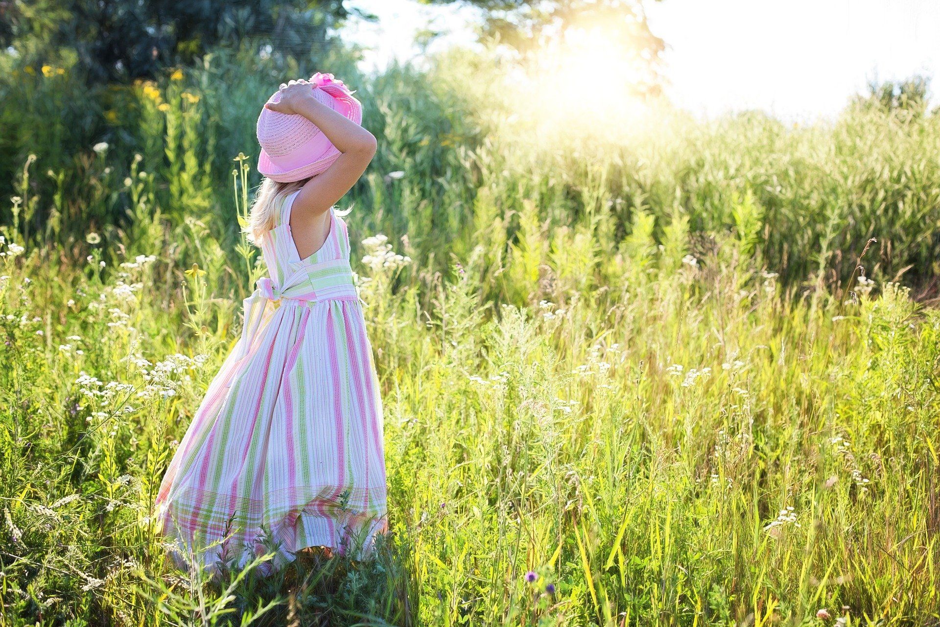 Ein kleines Mädchen in einem rosa Kleid und Hut steht auf einem Feld.