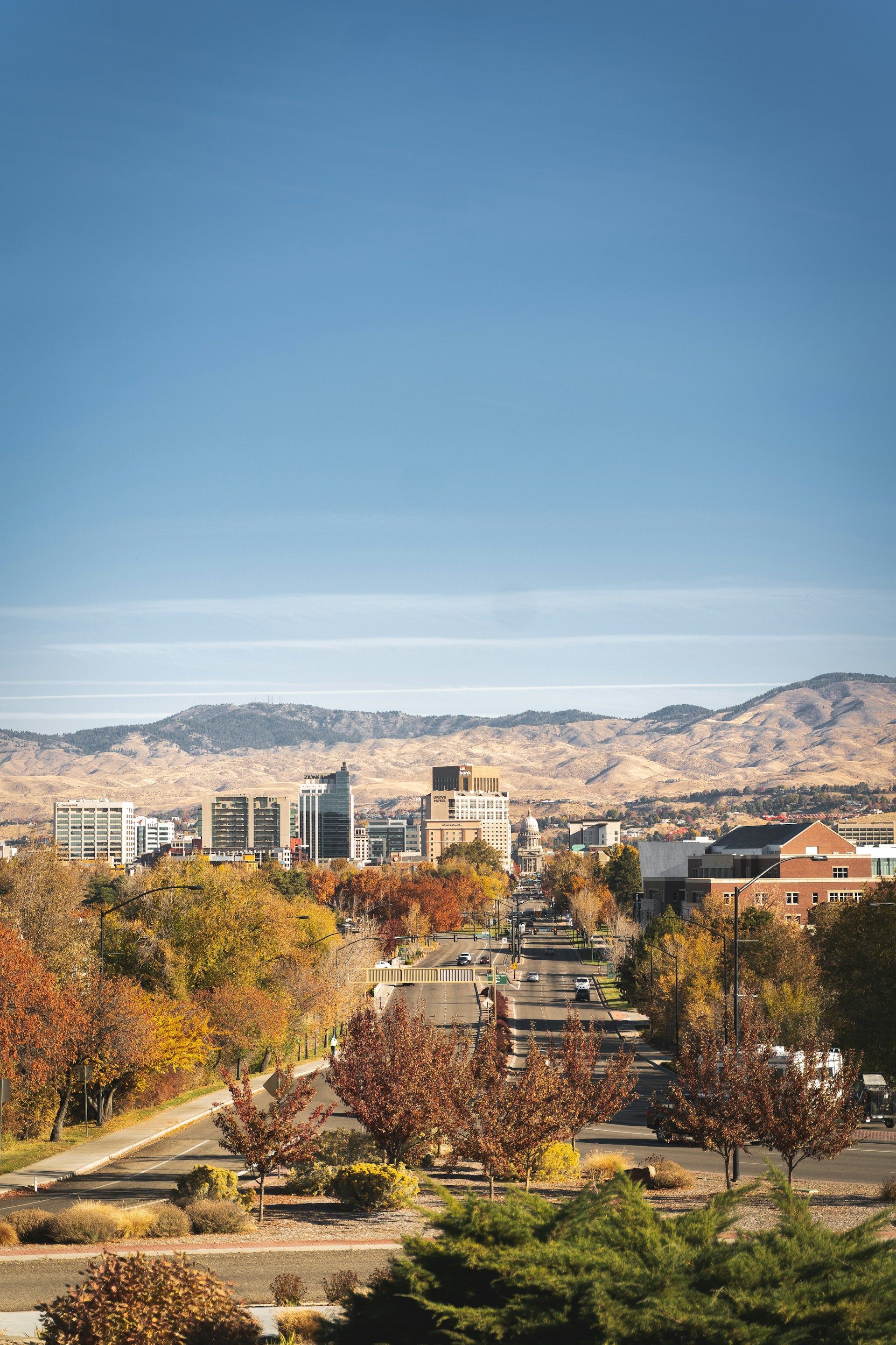 City skyline with autumn trees and mountains under a clear blue sky