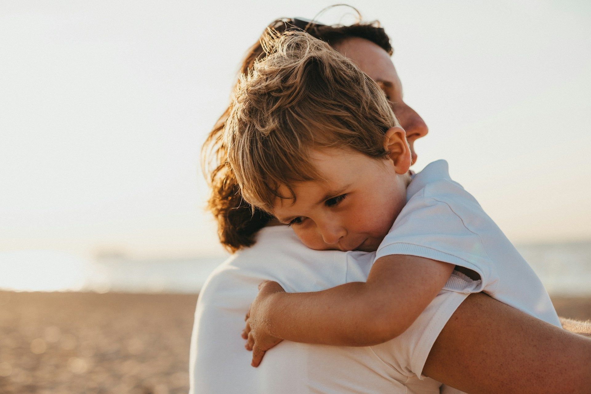 Person in white shirt hugging a child outdoors in warm sunlight