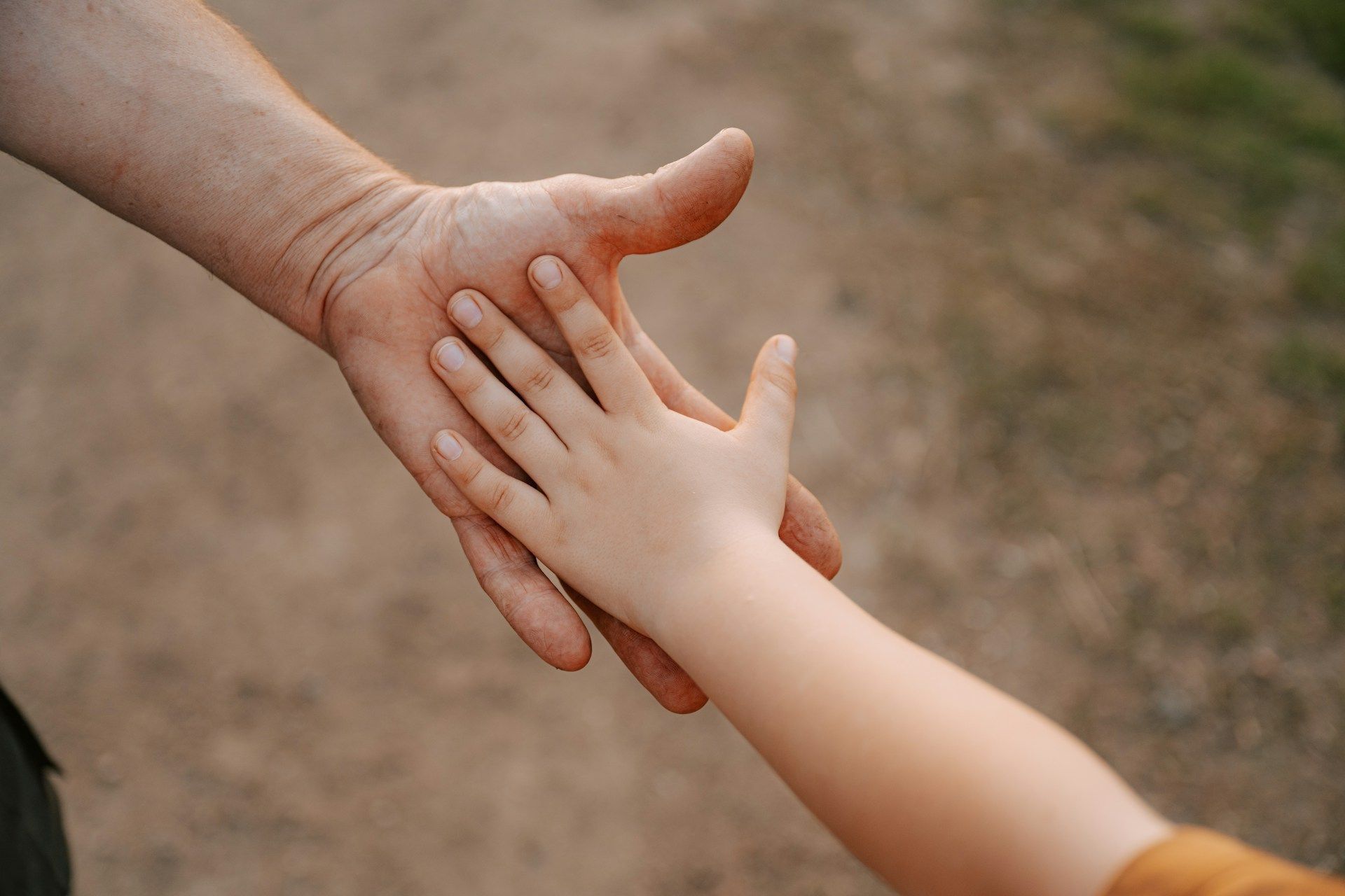 Adult and child hands reaching toward each other against a blurred outdoor background