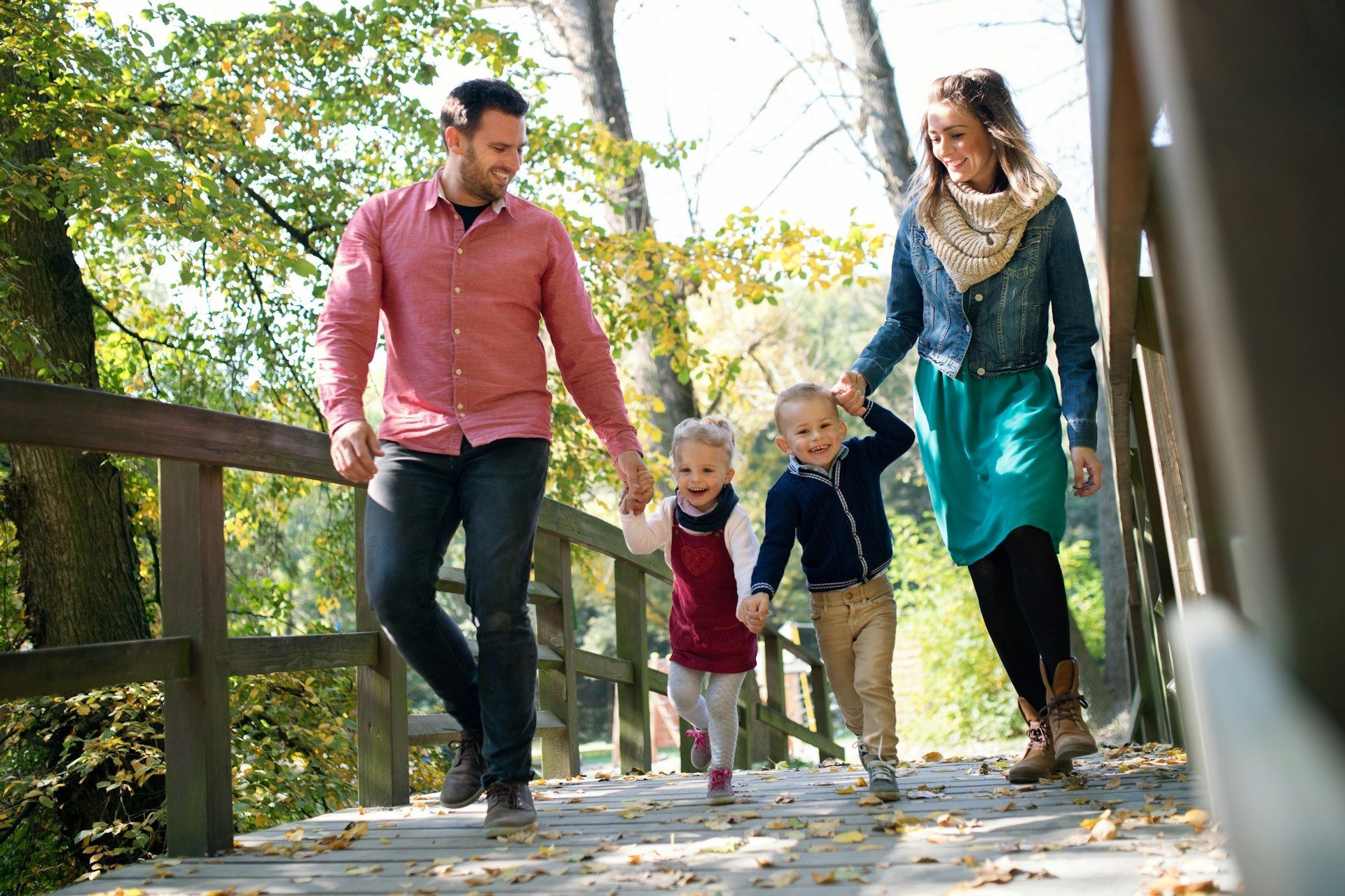 Family walking hand in hand on a sunlit park path with autumn leaves