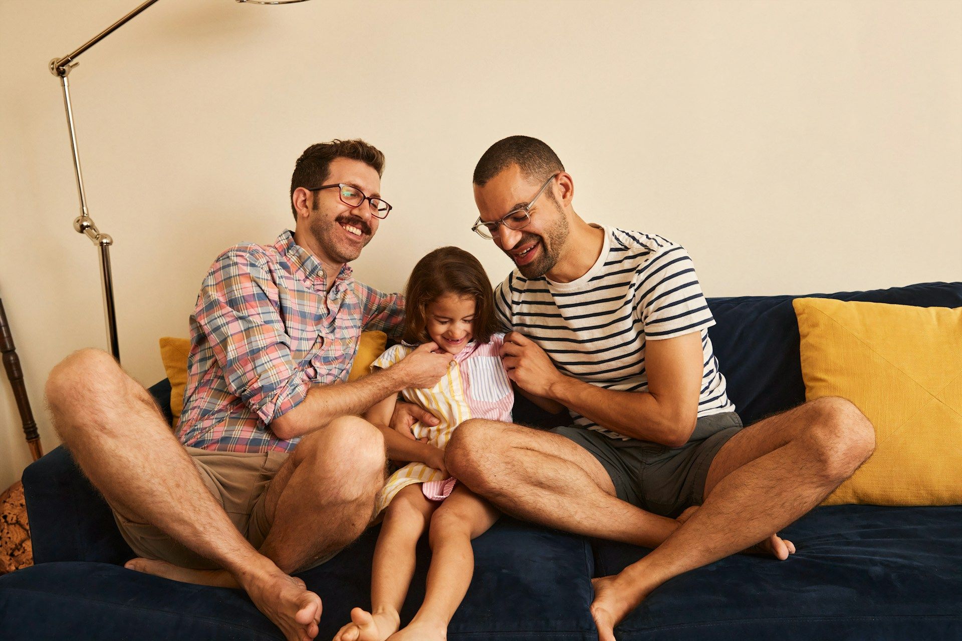 Two adults and a child sit on a couch, smiling at a phone together in a cozy living room.