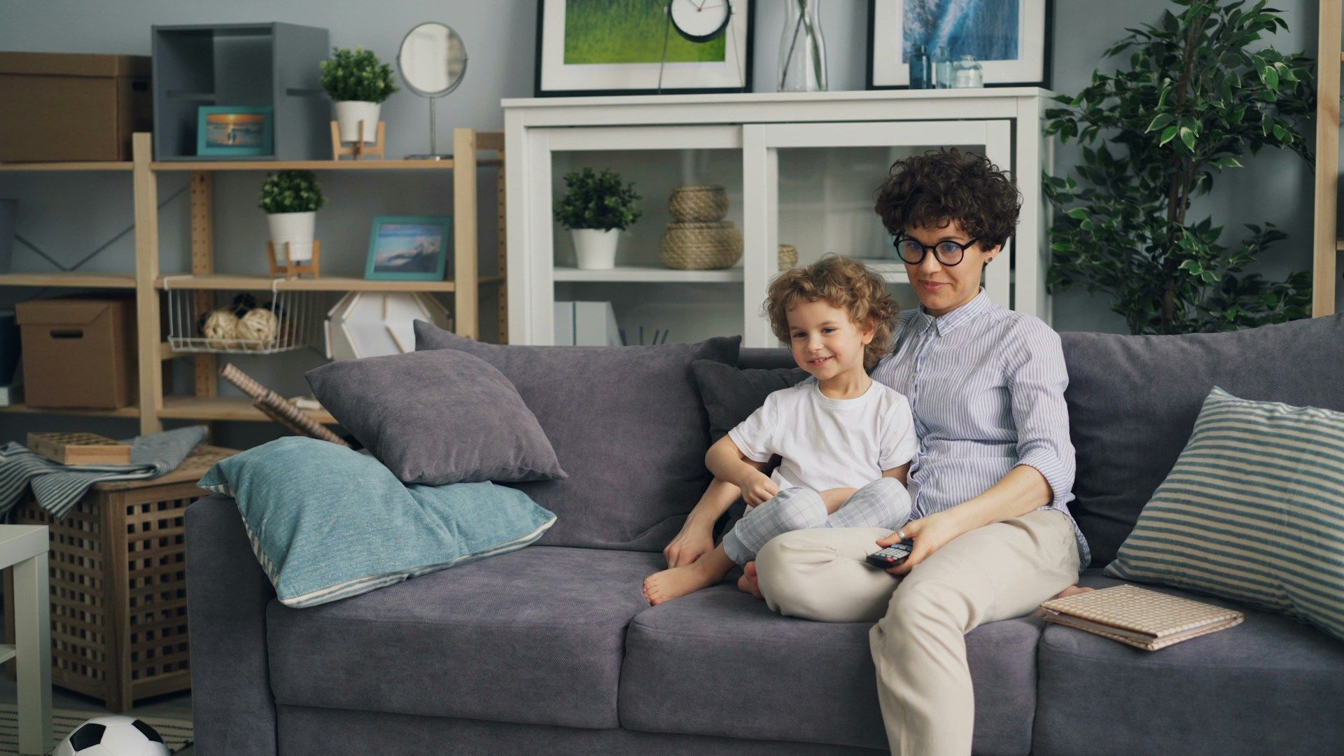 Adult and child sitting on a gray sofa in a bright living room, smiling and reading together