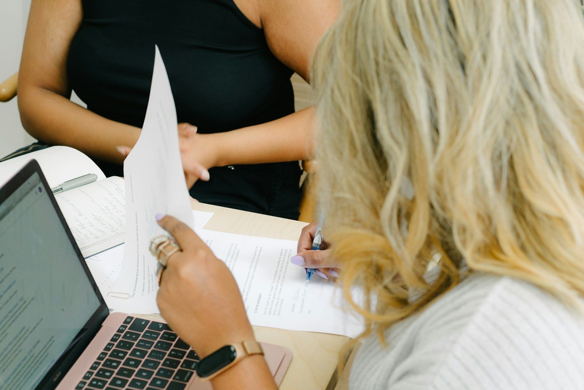 Two people reviewing documents at a table with a laptop and papers