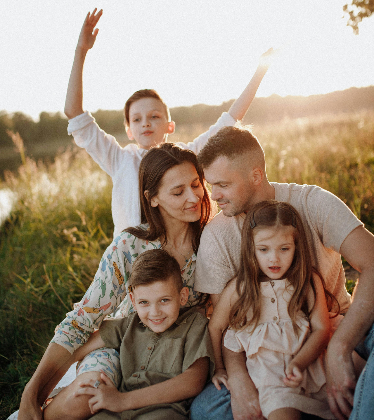 Family sitting together in a sunlit field, smiling and embracing during golden hour.