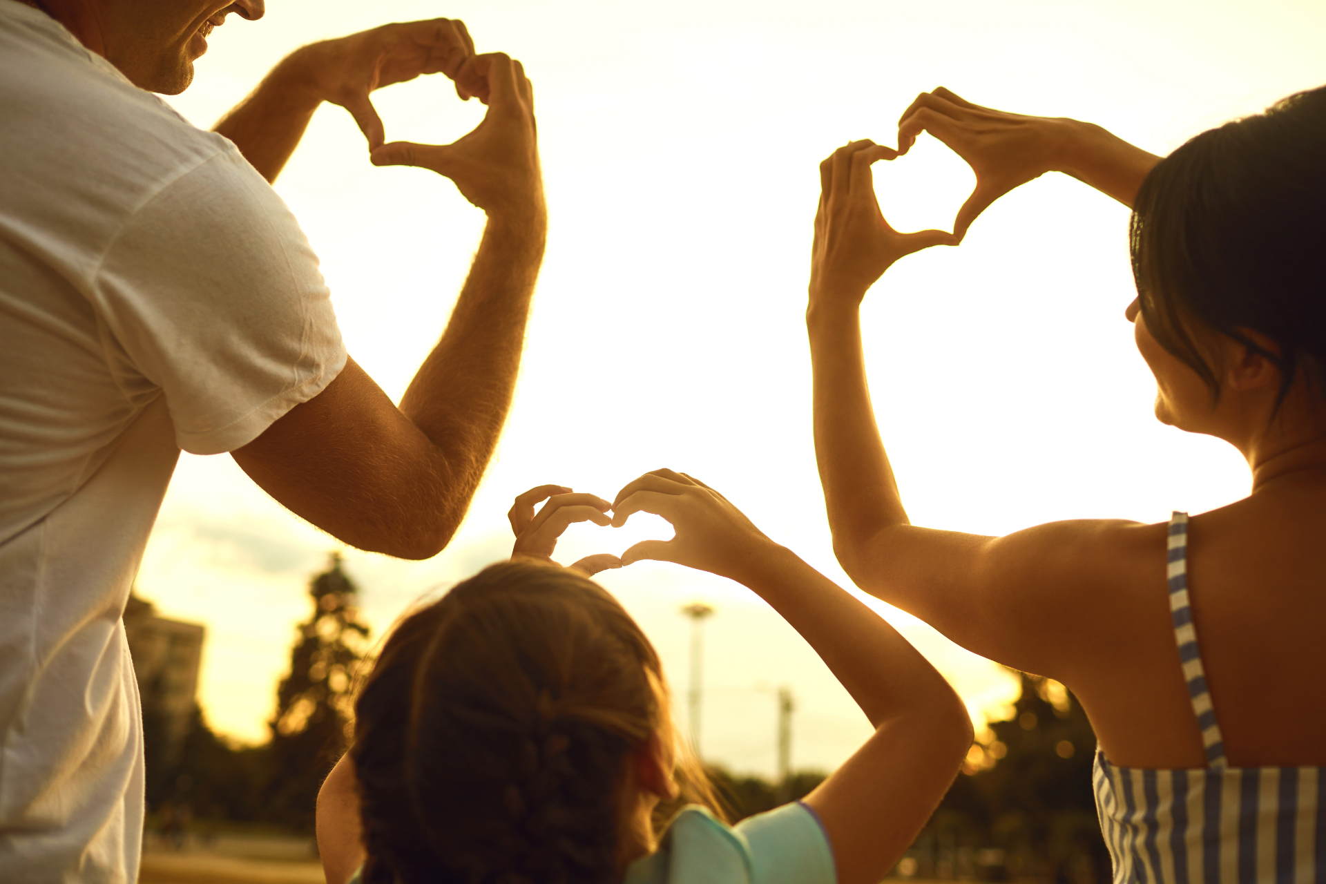 People making heart shapes with their hands at sunset outdoors